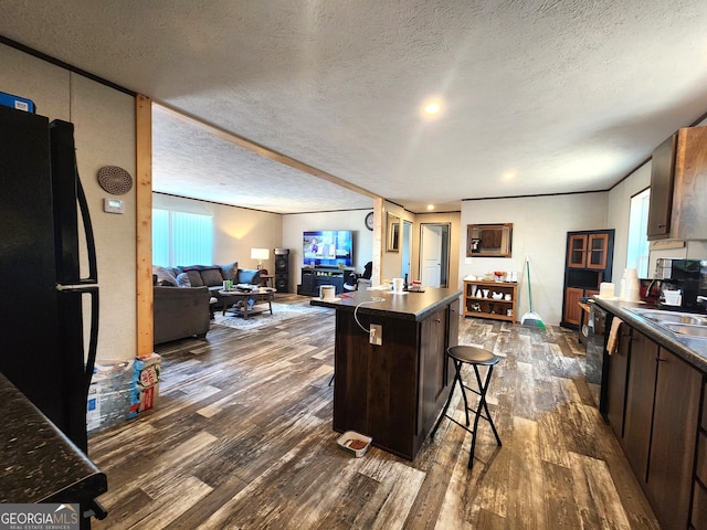 kitchen featuring dark brown cabinetry, black fridge, a textured ceiling, a breakfast bar, and a kitchen island