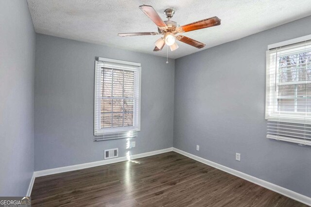 unfurnished room featuring ceiling fan, dark wood-type flooring, a healthy amount of sunlight, and a textured ceiling