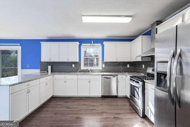 kitchen featuring white cabinets, decorative backsplash, light stone countertops, appliances with stainless steel finishes, and kitchen peninsula