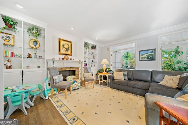 living room featuring built in shelves, a fireplace, wood-type flooring, and ornamental molding