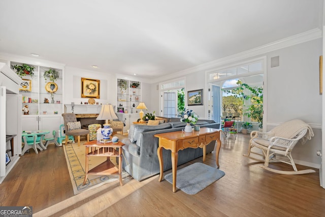 living room featuring built in shelves, crown molding, hardwood / wood-style floors, and a fireplace