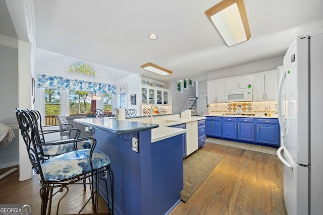 kitchen with a breakfast bar, white appliances, blue cabinets, sink, and white cabinetry