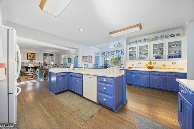 kitchen with white appliances, blue cabinetry, a center island with sink, white cabinets, and hardwood / wood-style floors