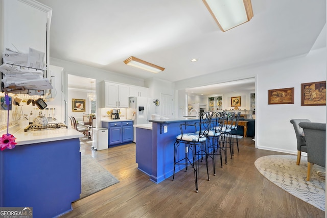 kitchen featuring blue cabinetry, white fridge with ice dispenser, dark hardwood / wood-style floors, a breakfast bar, and white cabinets