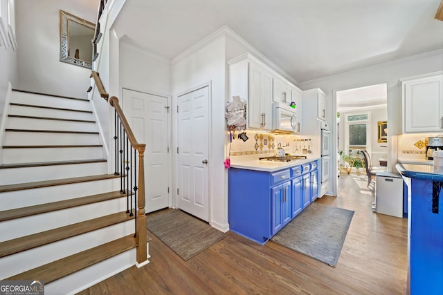 kitchen with decorative backsplash, appliances with stainless steel finishes, blue cabinets, hardwood / wood-style flooring, and white cabinets