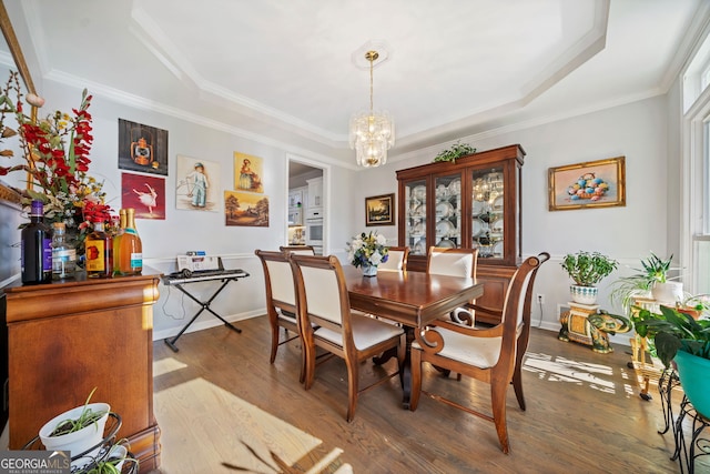 dining room featuring a raised ceiling, ornamental molding, wood-type flooring, and a notable chandelier