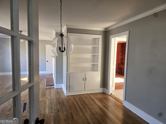 unfurnished dining area featuring a chandelier, built in shelves, crown molding, and dark wood-type flooring