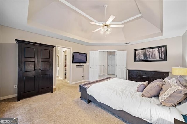 carpeted bedroom with a tray ceiling, ensuite bath, and ceiling fan