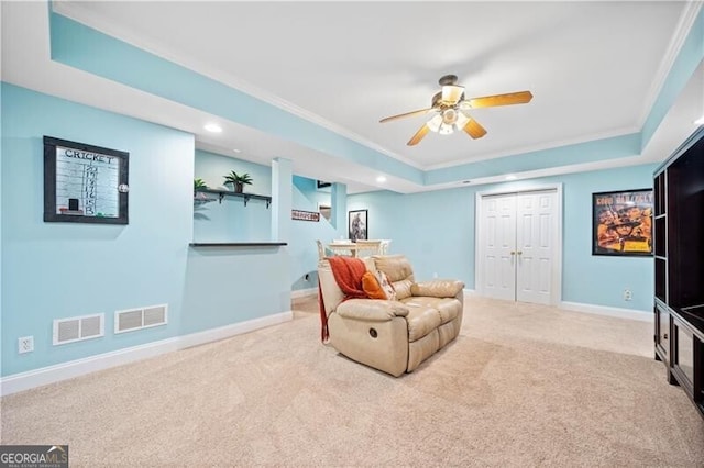 sitting room with a raised ceiling, light carpet, and ornamental molding