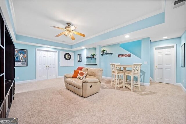 carpeted living room with ceiling fan, crown molding, and a tray ceiling