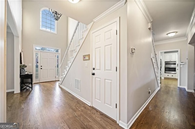 foyer entrance with dark wood-type flooring, ornamental molding, and an inviting chandelier