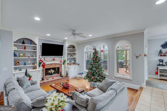 living room with ornamental molding, built in shelves, ceiling fan, light hardwood / wood-style flooring, and a fireplace