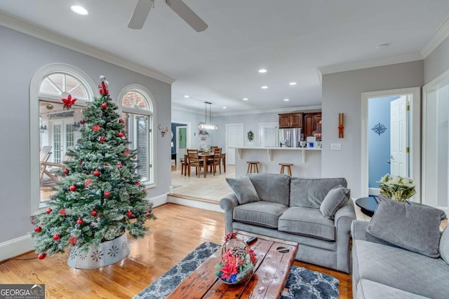 living room featuring ceiling fan with notable chandelier, light wood-type flooring, and ornamental molding