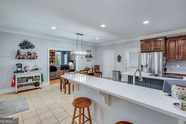 kitchen with pendant lighting, ornamental molding, tasteful backsplash, stainless steel fridge with ice dispenser, and a breakfast bar area