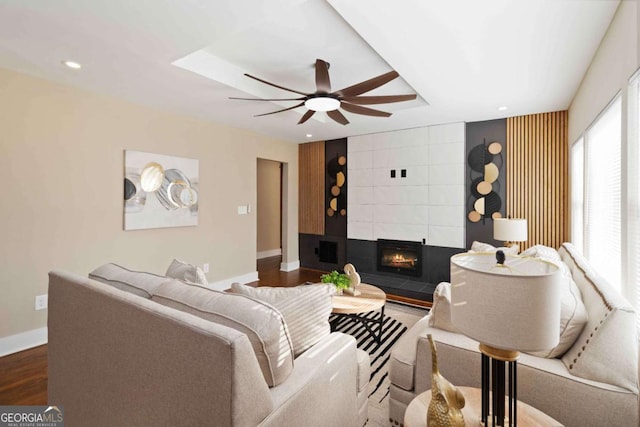 living room with a tray ceiling, ceiling fan, a fireplace, and hardwood / wood-style flooring