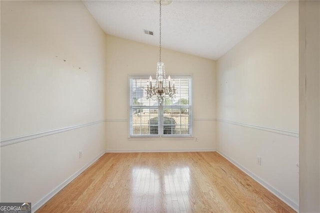 unfurnished dining area featuring a chandelier, light hardwood / wood-style flooring, and vaulted ceiling