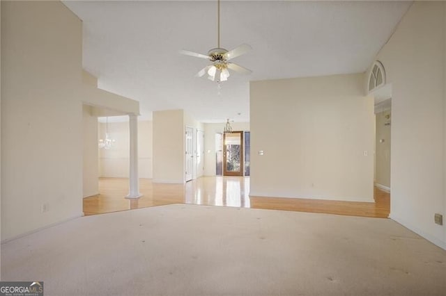 carpeted empty room featuring ornate columns and ceiling fan with notable chandelier