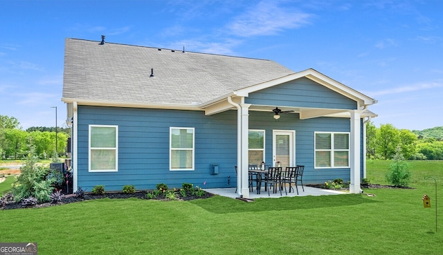 back of property with ceiling fan, a yard, roof with shingles, and a patio area