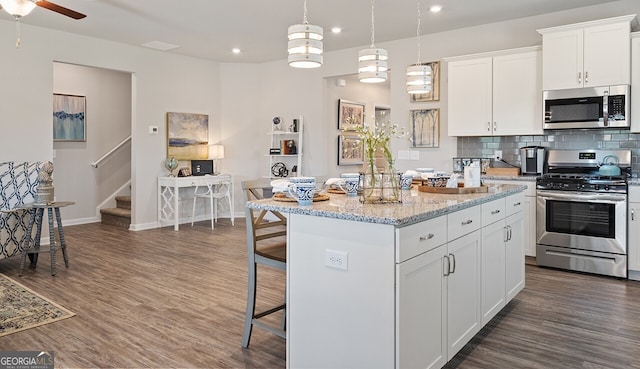 kitchen featuring a kitchen island, appliances with stainless steel finishes, a kitchen breakfast bar, dark wood-type flooring, and backsplash