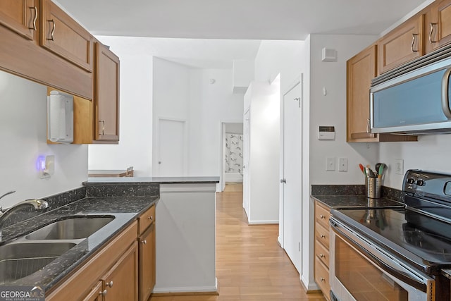 kitchen featuring dark stone countertops, sink, light wood-type flooring, and appliances with stainless steel finishes