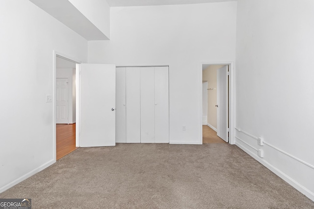 unfurnished bedroom with a towering ceiling, light carpet, and a closet