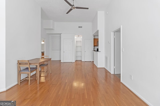 interior space featuring ceiling fan, light wood-type flooring, and a towering ceiling