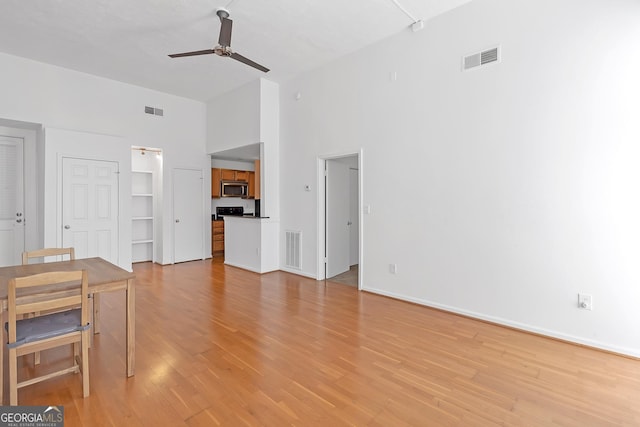 unfurnished living room featuring a high ceiling, light wood-type flooring, and ceiling fan