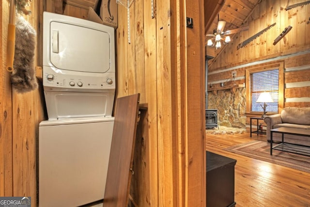 laundry room featuring wood ceiling, wooden walls, wood-type flooring, stacked washer and dryer, and a wood stove