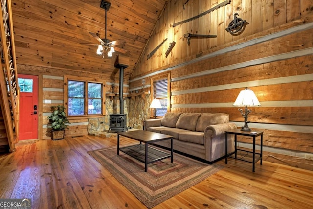 living room with a wood stove, ceiling fan, wooden walls, and hardwood / wood-style flooring