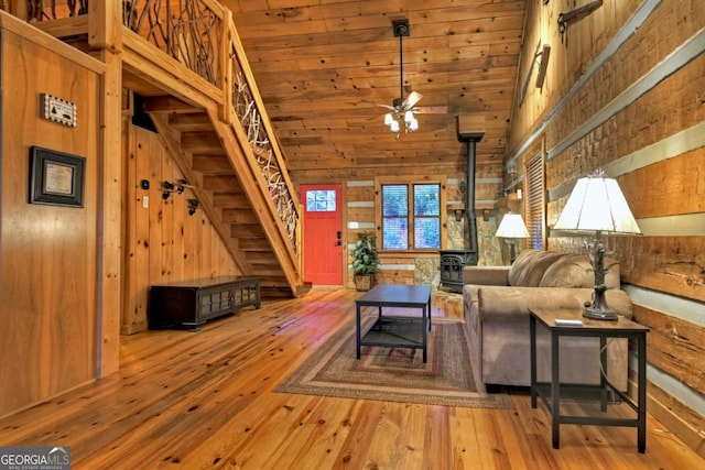 living room with ceiling fan, wood walls, light wood-type flooring, and high vaulted ceiling