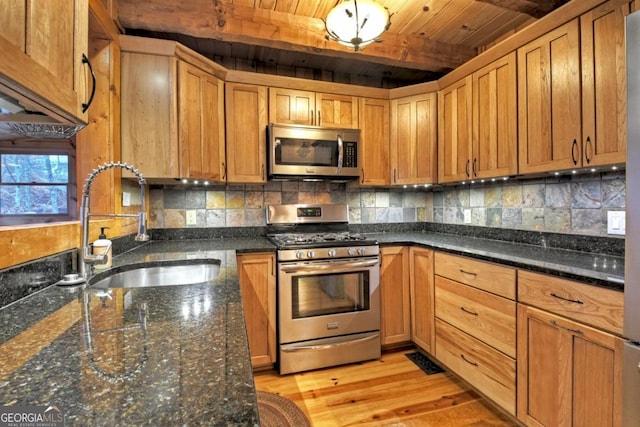 kitchen with stainless steel appliances, sink, dark stone countertops, beamed ceiling, and light hardwood / wood-style floors