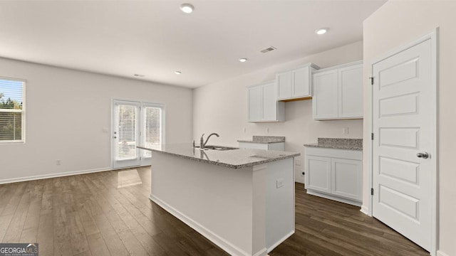 kitchen with light stone countertops, dark hardwood / wood-style flooring, white cabinetry, and a kitchen island with sink