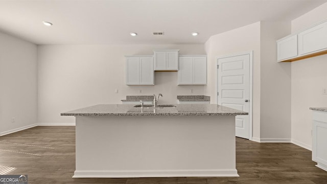 kitchen with light stone countertops, white cabinetry, and an island with sink