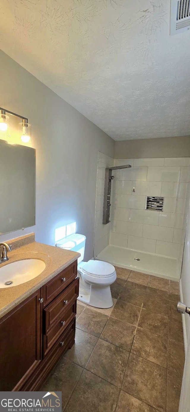 bathroom with tiled shower, vanity, a textured ceiling, and toilet