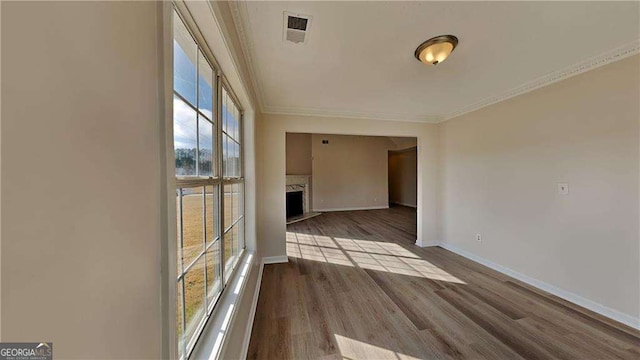 empty room with a high end fireplace, light hardwood / wood-style floors, ornamental molding, and a wealth of natural light