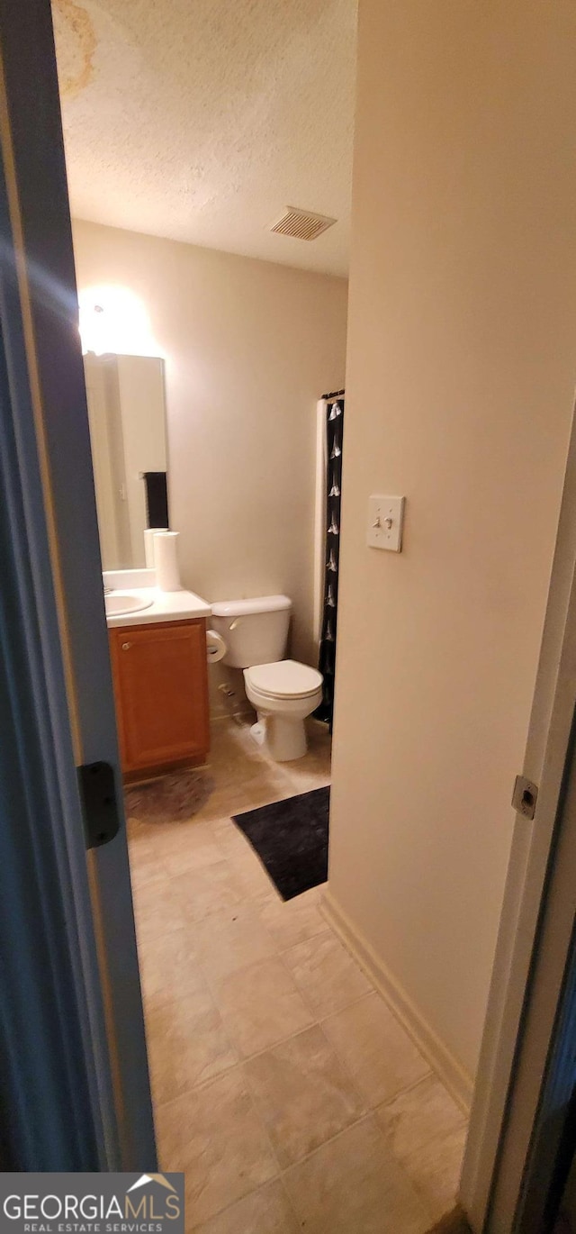 bathroom with a textured ceiling, vanity, and toilet