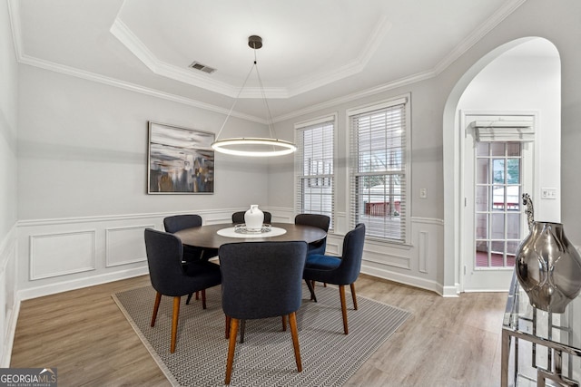 dining space with light wood-type flooring, a raised ceiling, and ornamental molding