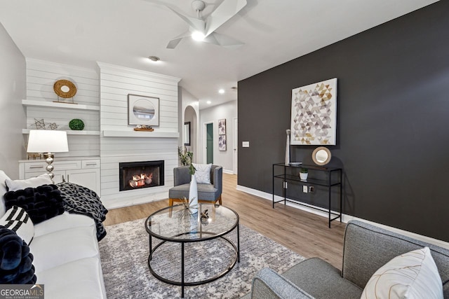 living room featuring ceiling fan, a large fireplace, and light hardwood / wood-style floors