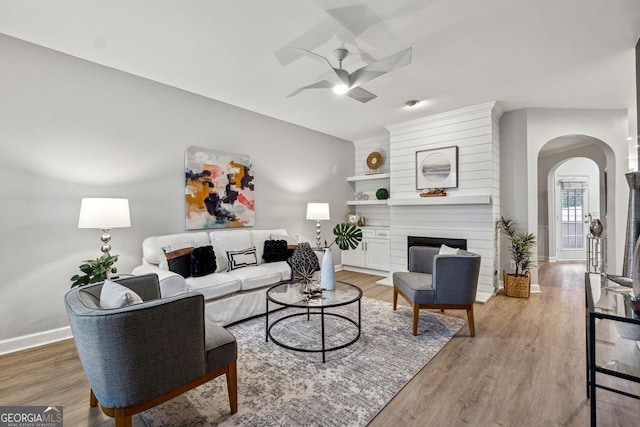 living room with light wood-type flooring, a large fireplace, and ceiling fan