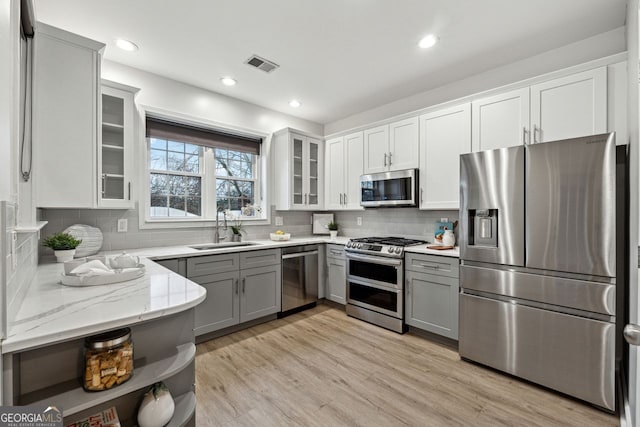 kitchen with gray cabinetry, sink, light hardwood / wood-style floors, light stone counters, and stainless steel appliances