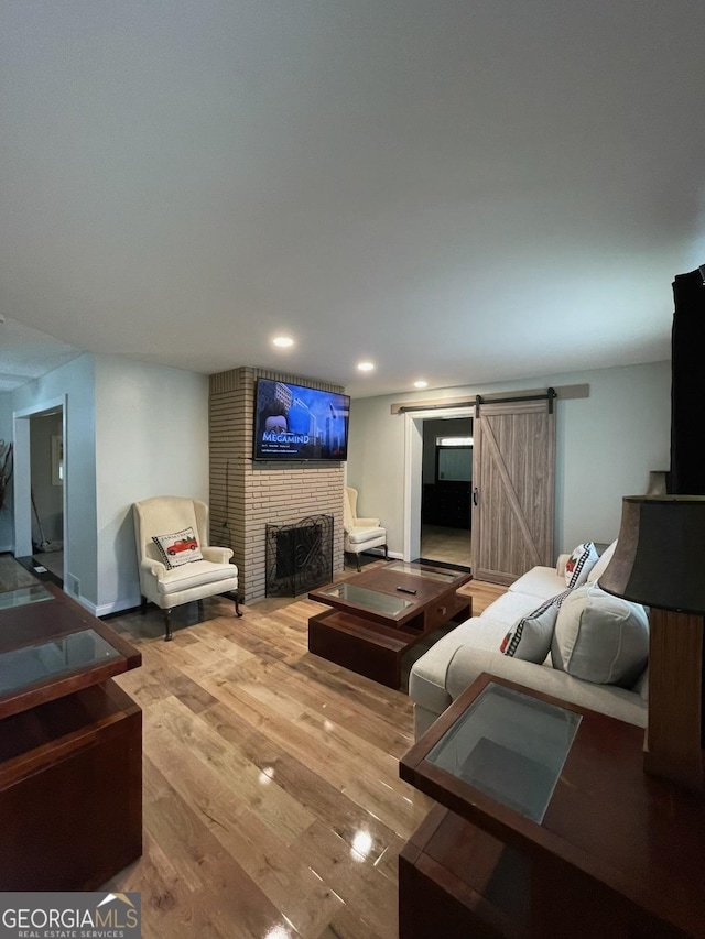 living room featuring a barn door, a brick fireplace, and hardwood / wood-style flooring