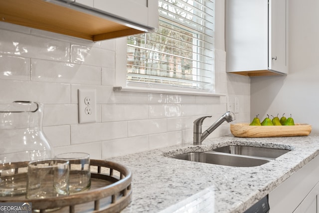 kitchen with light stone countertops, backsplash, white cabinetry, and sink