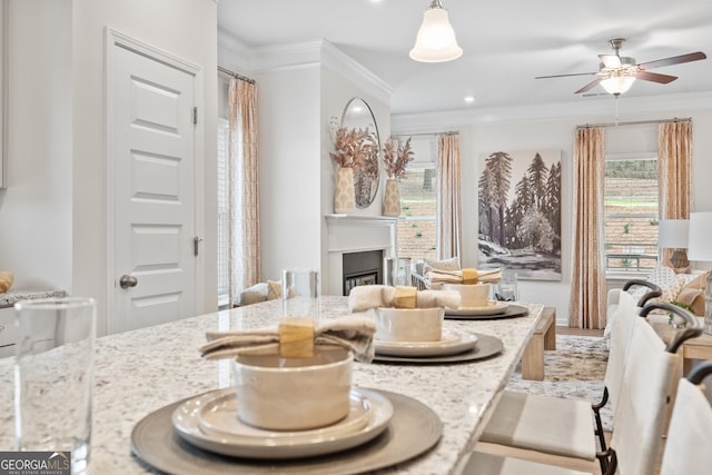 dining space with ornamental molding, a ceiling fan, and a glass covered fireplace