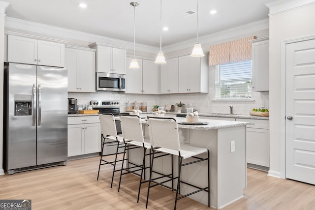 kitchen with hanging light fixtures, appliances with stainless steel finishes, white cabinetry, and a kitchen island with sink