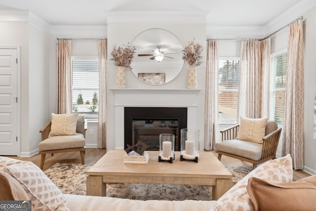 living area with a glass covered fireplace, wood finished floors, a wealth of natural light, and crown molding