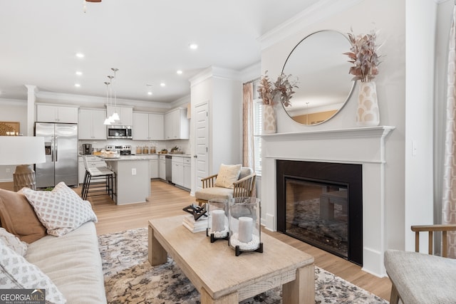 living area featuring light wood-type flooring, recessed lighting, crown molding, and a glass covered fireplace