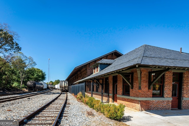 view of property exterior featuring roof with shingles, fence, and brick siding