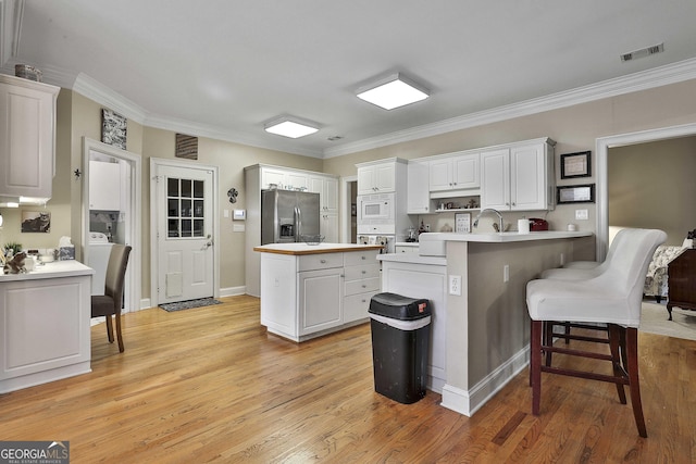 kitchen featuring white appliances, light wood-type flooring, a kitchen island, a kitchen bar, and white cabinetry