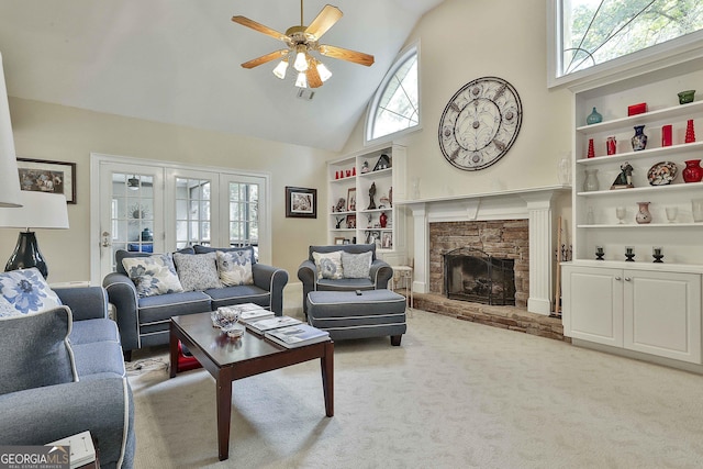 carpeted living room with ceiling fan, a stone fireplace, and high vaulted ceiling