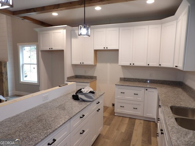 kitchen featuring beam ceiling, white cabinetry, light stone counters, pendant lighting, and light hardwood / wood-style floors